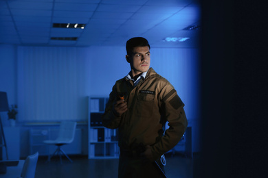 Professional security guard with portable radio set in dark office