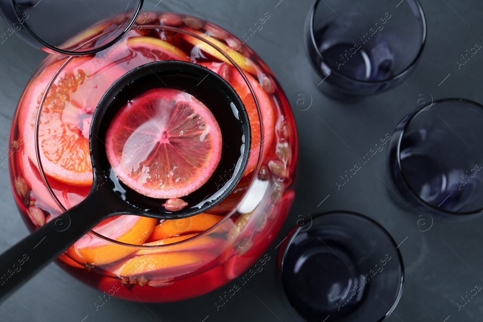 Photo of Ladle with aromatic punch drink above glass bowl on black table, top view