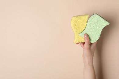 Woman holding sponges on beige background, top view. Space for text