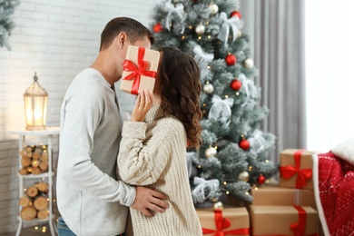 Couple kissing while hiding behind Christmas gift at home