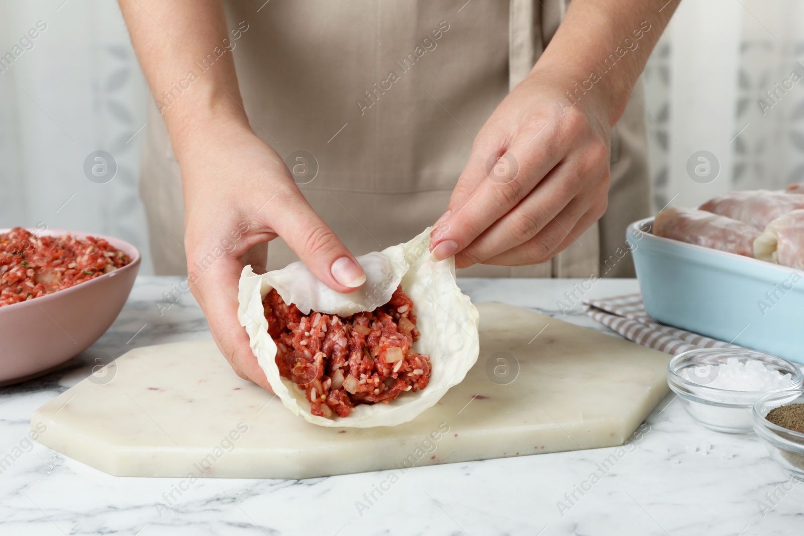 Photo of Woman preparing stuffed cabbage rolls at white marble table, closeup