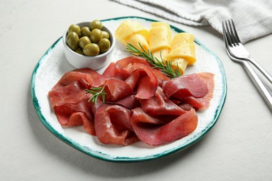 Photo of Delicious bresaola, cheese, olives and rosemary on light textured table