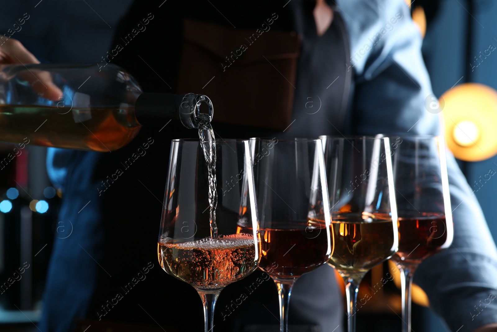 Photo of Bartender pouring rose wine from bottle into glass indoors, closeup