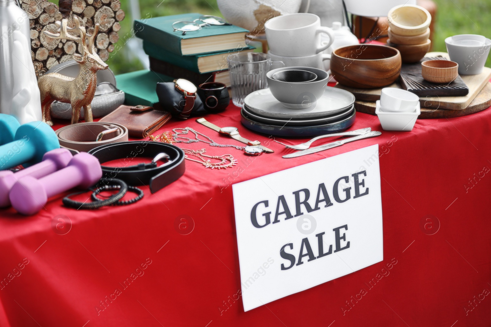 Photo of Paper with sign Garage sale and many different items on red tablecloth outdoors