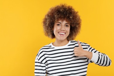Photo of Woman with clean teeth showing thumbs up on yellow background, space for text