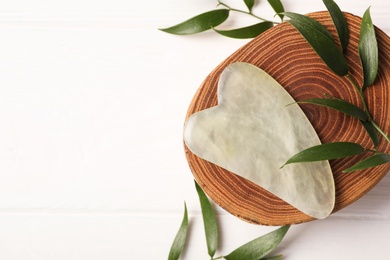 Photo of Jade gua sha tool and green branches on white wooden table, flat lay. Space for text