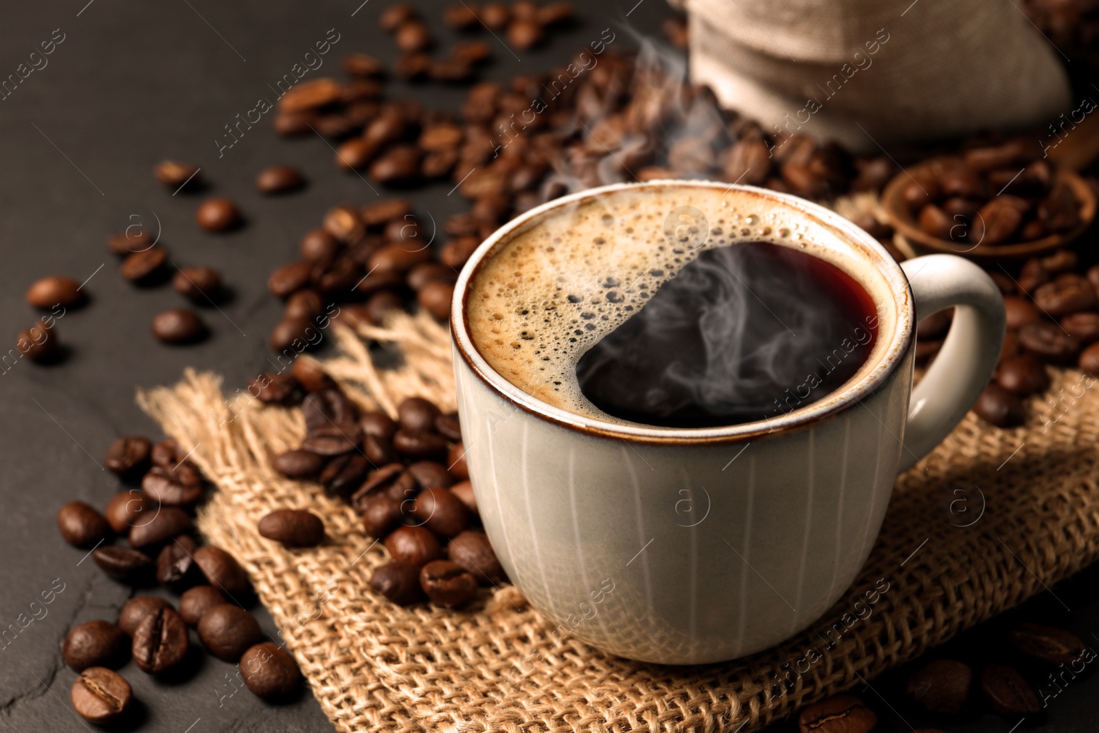 Image of Cup of aromatic hot coffee and beans on black table, closeup