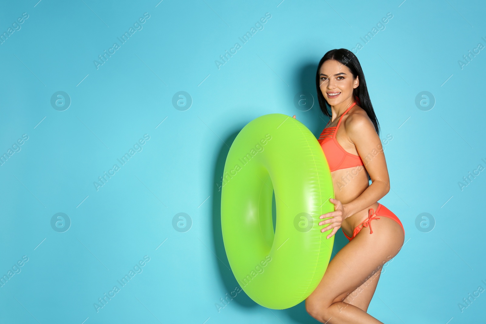 Photo of Beautiful young woman in stylish bikini with green inflatable ring on light blue background. Space for text