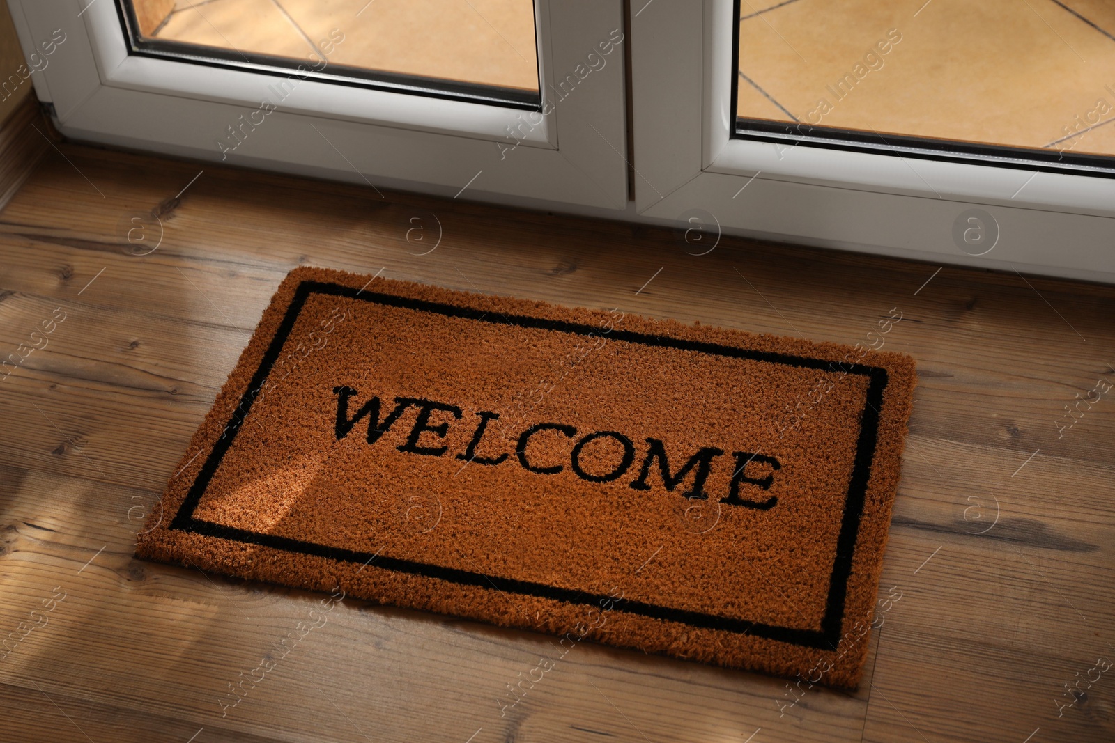 Photo of Door mat with word Welcome on wooden floor near entrance