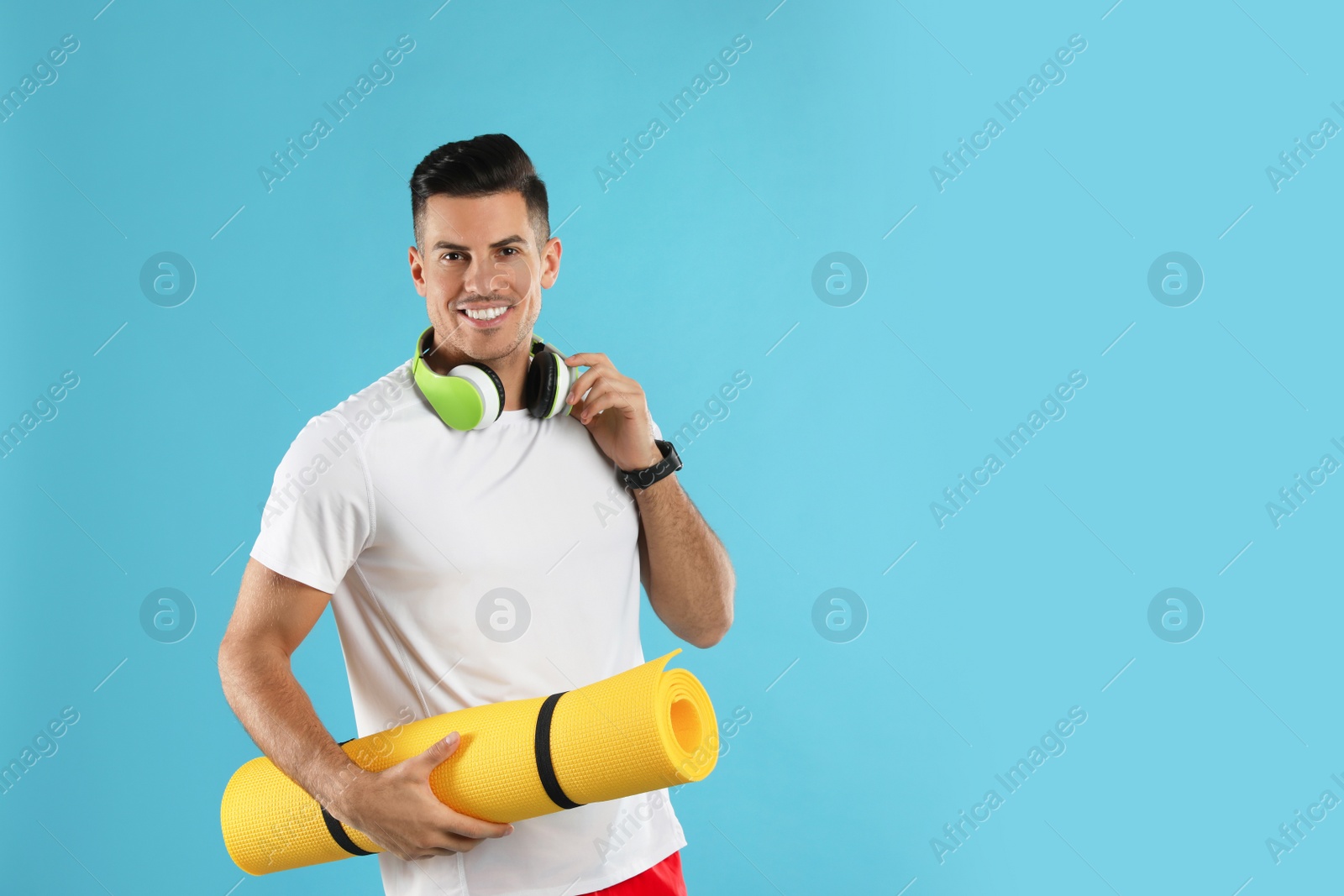Photo of Handsome man with yoga mat and headphones on turquoise background. Space for text