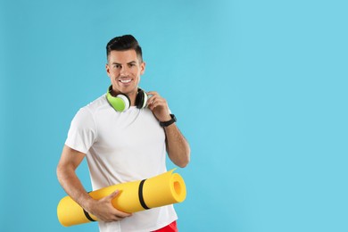 Handsome man with yoga mat and headphones on turquoise background. Space for text