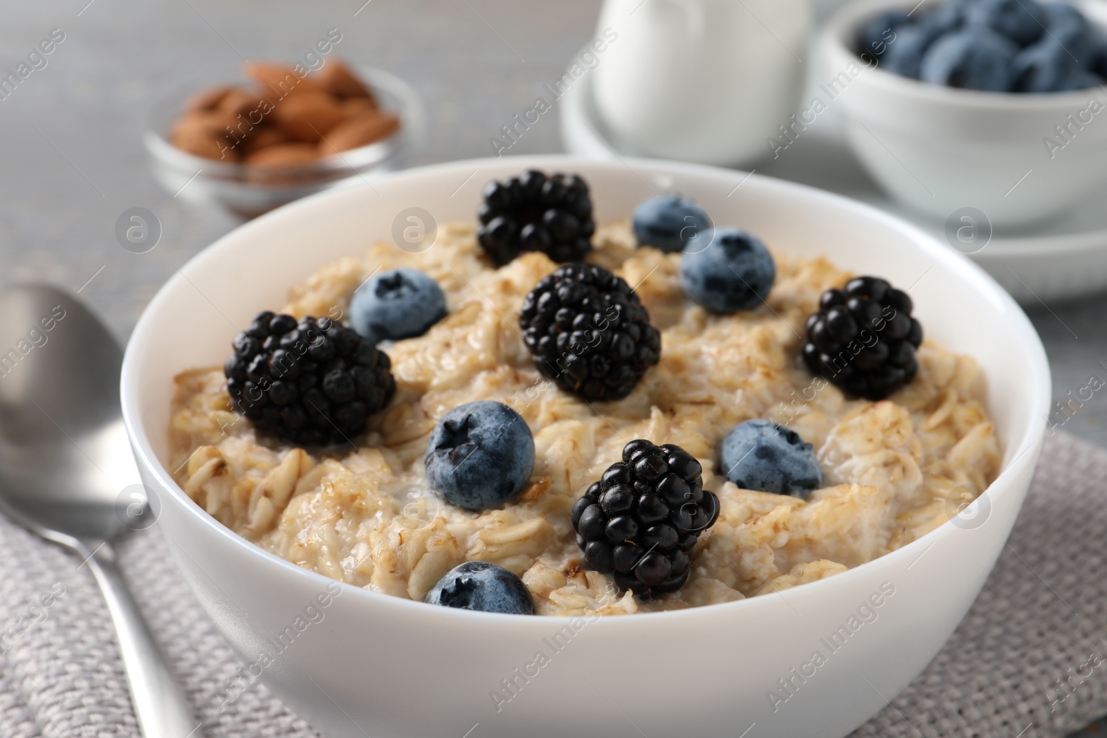 Photo of Tasty oatmeal porridge with blackberries and blueberries in bowl on table, closeup