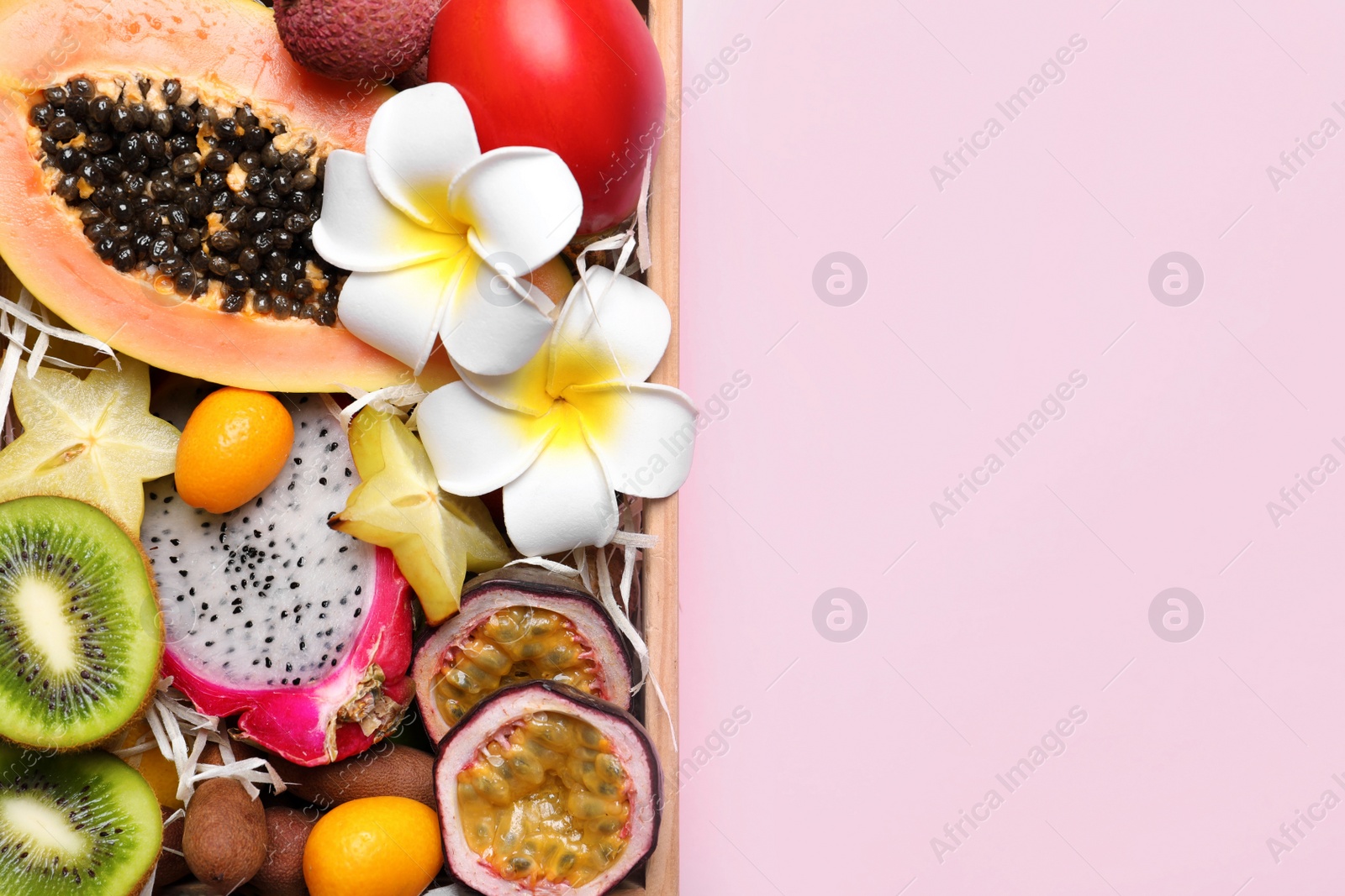 Photo of Different tropical fruits in wooden box on pink background, top view. Space for text