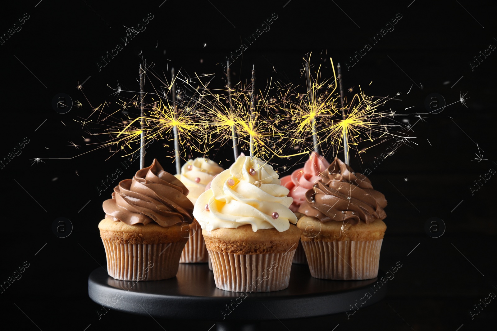 Image of Birthday cupcakes with sparklers on stand against dark background