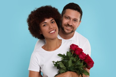 International dating. Happy couple with bouquet of roses on light blue background