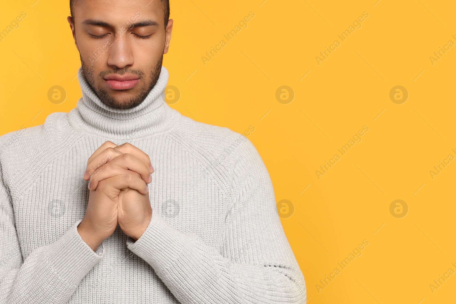 Photo of African American man with clasped hands praying to God on orange background. Space for text