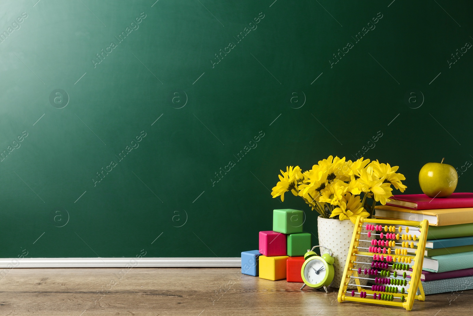 Photo of Vase of flowers, books and toys on wooden table near green chalkboard, space for text. Teacher's day