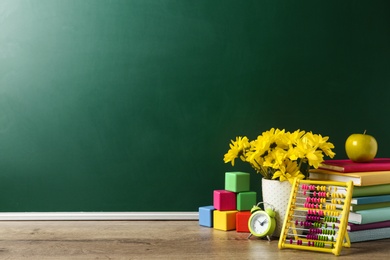 Photo of Vase of flowers, books and toys on wooden table near green chalkboard, space for text. Teacher's day