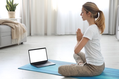 Photo of Woman having online video class via laptop at home. Distance yoga course during coronavirus pandemic