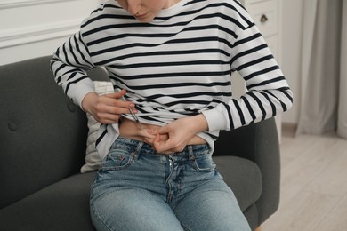 Photo of Diabetes. Woman making insulin injection into her belly on sofa indoors, closeup