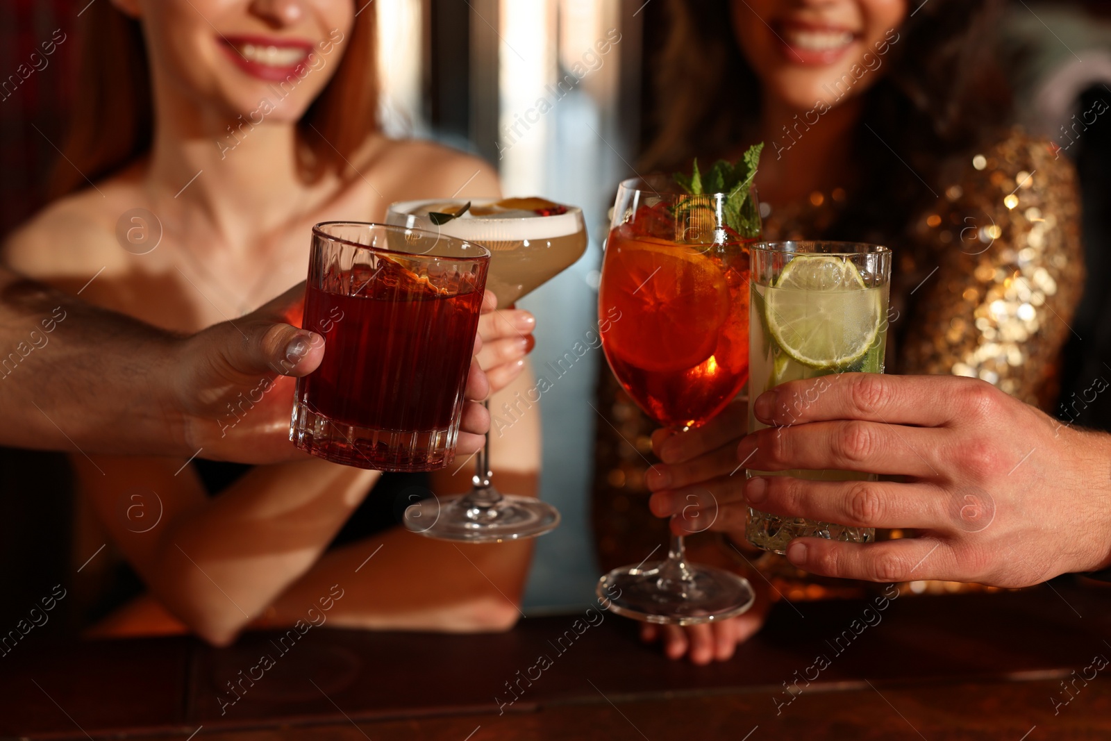 Photo of Friends clinking glasses with fresh cocktails in bar, closeup