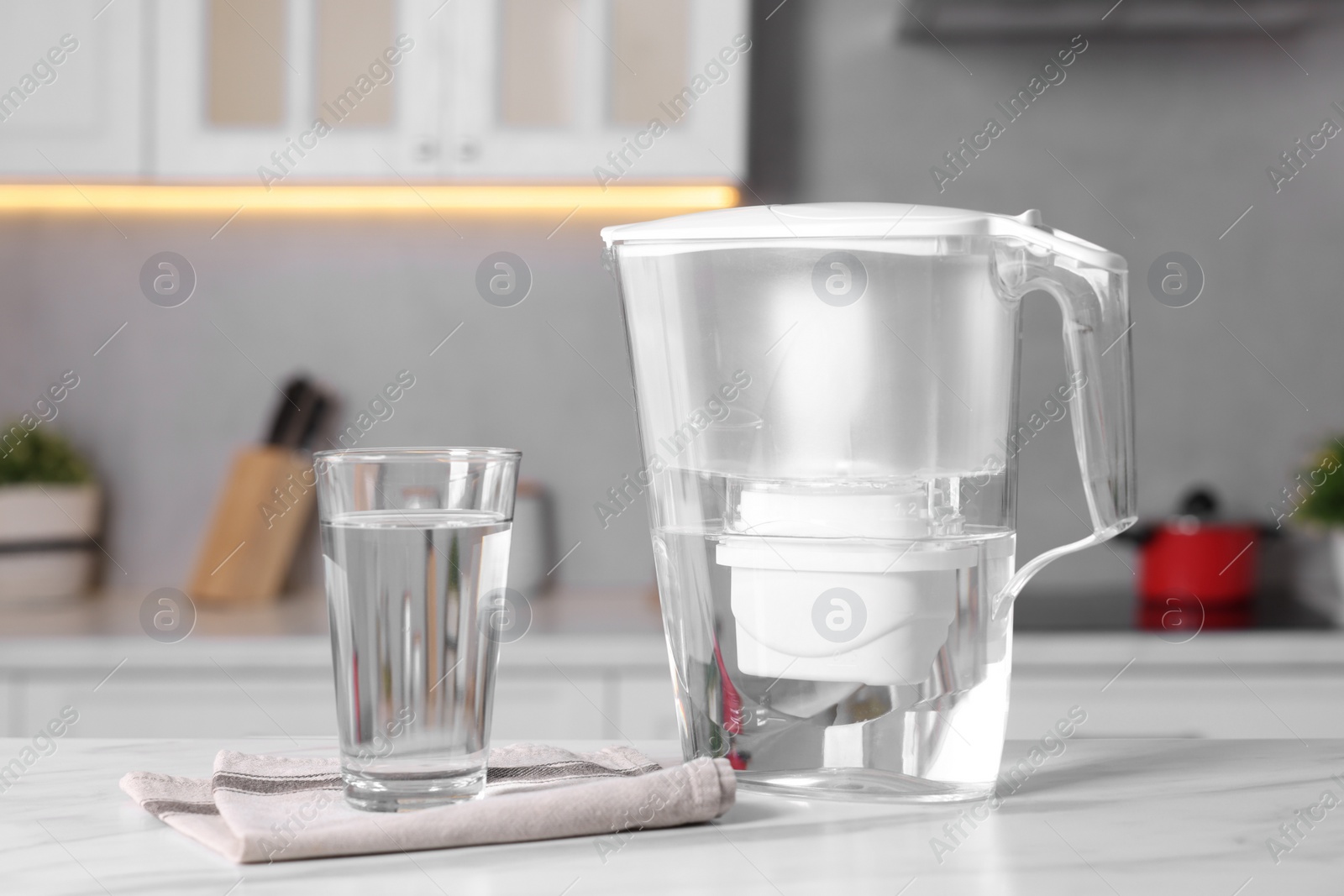 Photo of Water filter jug and glass on white marble table in kitchen, closeup