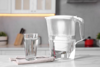 Water filter jug and glass on white marble table in kitchen, closeup