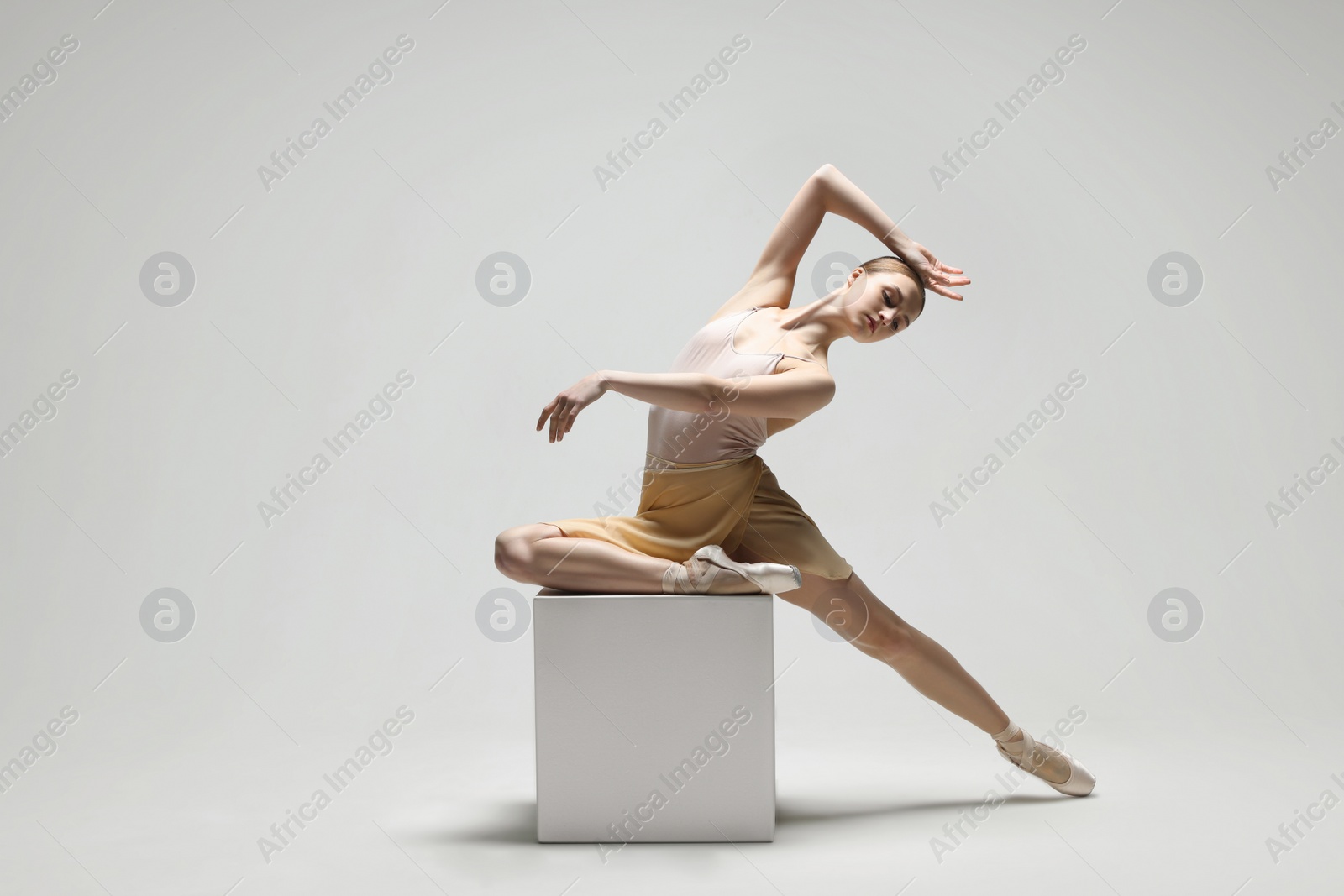 Photo of Young ballerina practicing dance moves on cube against white background. Space for text