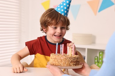 Birthday celebration. Mother holding tasty cake near her son indoors