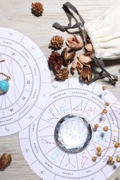 Photo of Astrology prediction. Zodiac wheels, gemstone and pouch with dry flowers on wooden table, flat lay