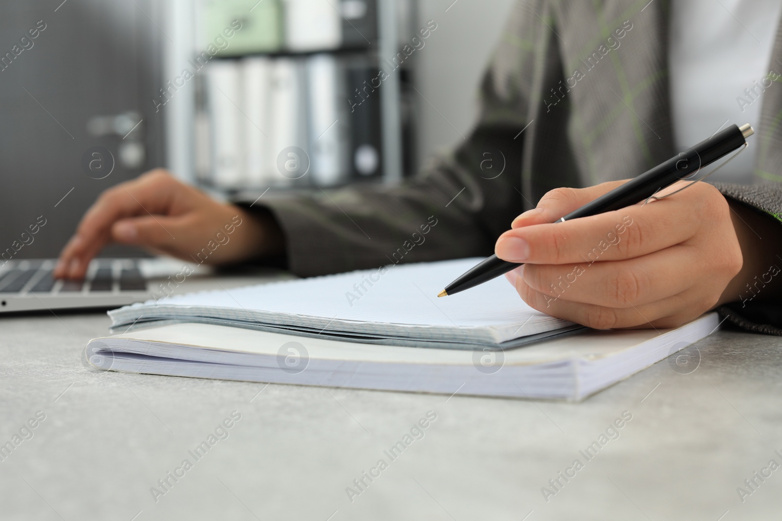 Photo of Woman working with laptop and writing in notebook at table indoors, closeup