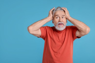 Photo of Portrait of surprised senior man on light blue background, space for text