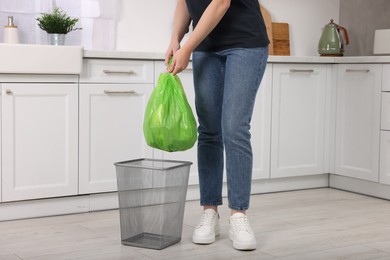 Photo of Woman taking garbage bag out of trash bin in kitchen, closeup