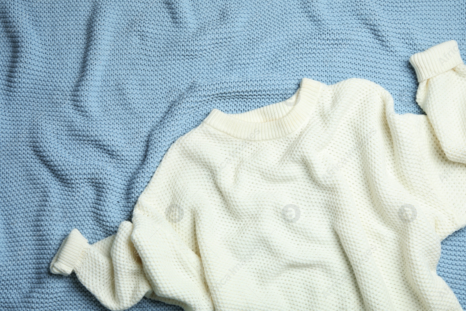 Photo of Warm white knitted sweater on light blue blanket, flat lay