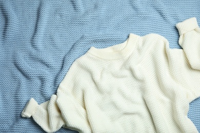 Warm white knitted sweater on light blue blanket, flat lay