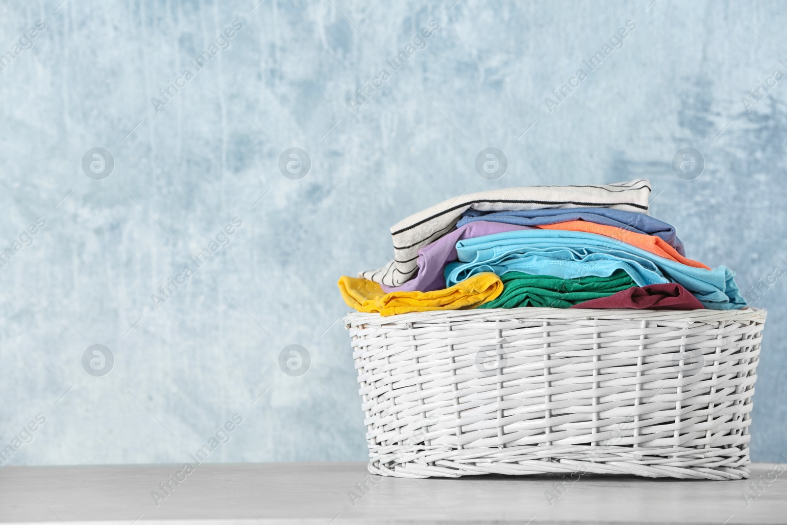 Photo of Basket with clean laundry on table against color background, space for text