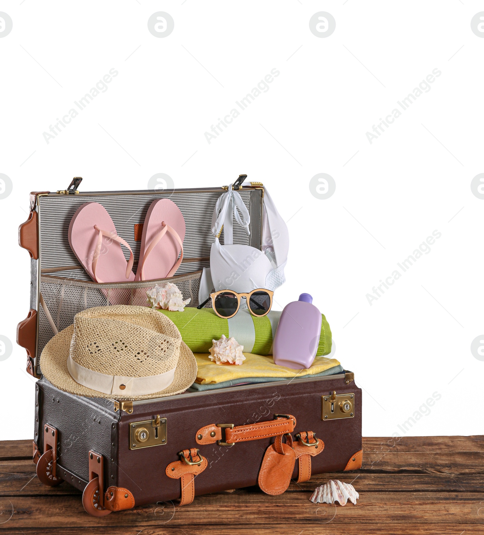 Photo of Open vintage suitcase with different beach objects packed for summer vacation on wooden table against white background