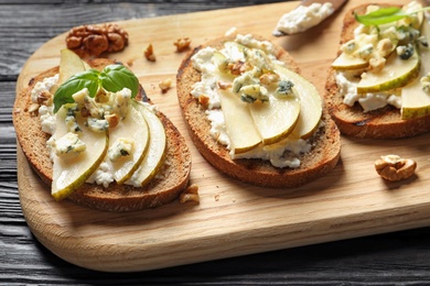 Photo of Wooden board with delicious pear bruschettas on table, closeup