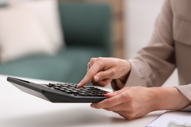 Woman using calculator at table indoors, closeup