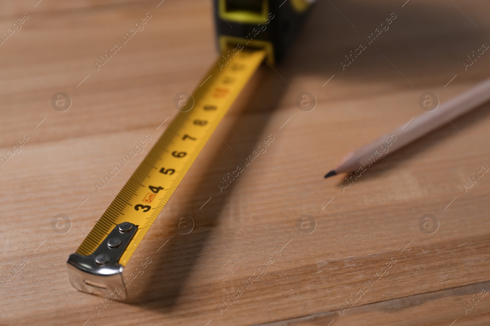 Photo of Self retracting metal measuring tape and pencil on wooden table, closeup
