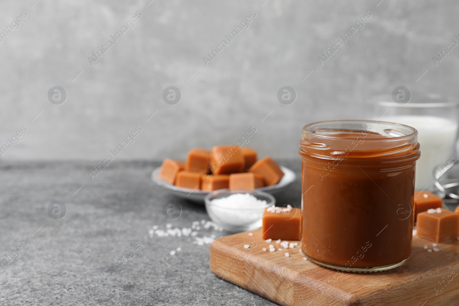 Photo of Yummy salted caramel in glass jar and candies on grey table, space for text