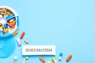Photo of Card with word Rheumatism and pills on light blue background, flat lay. Space for text