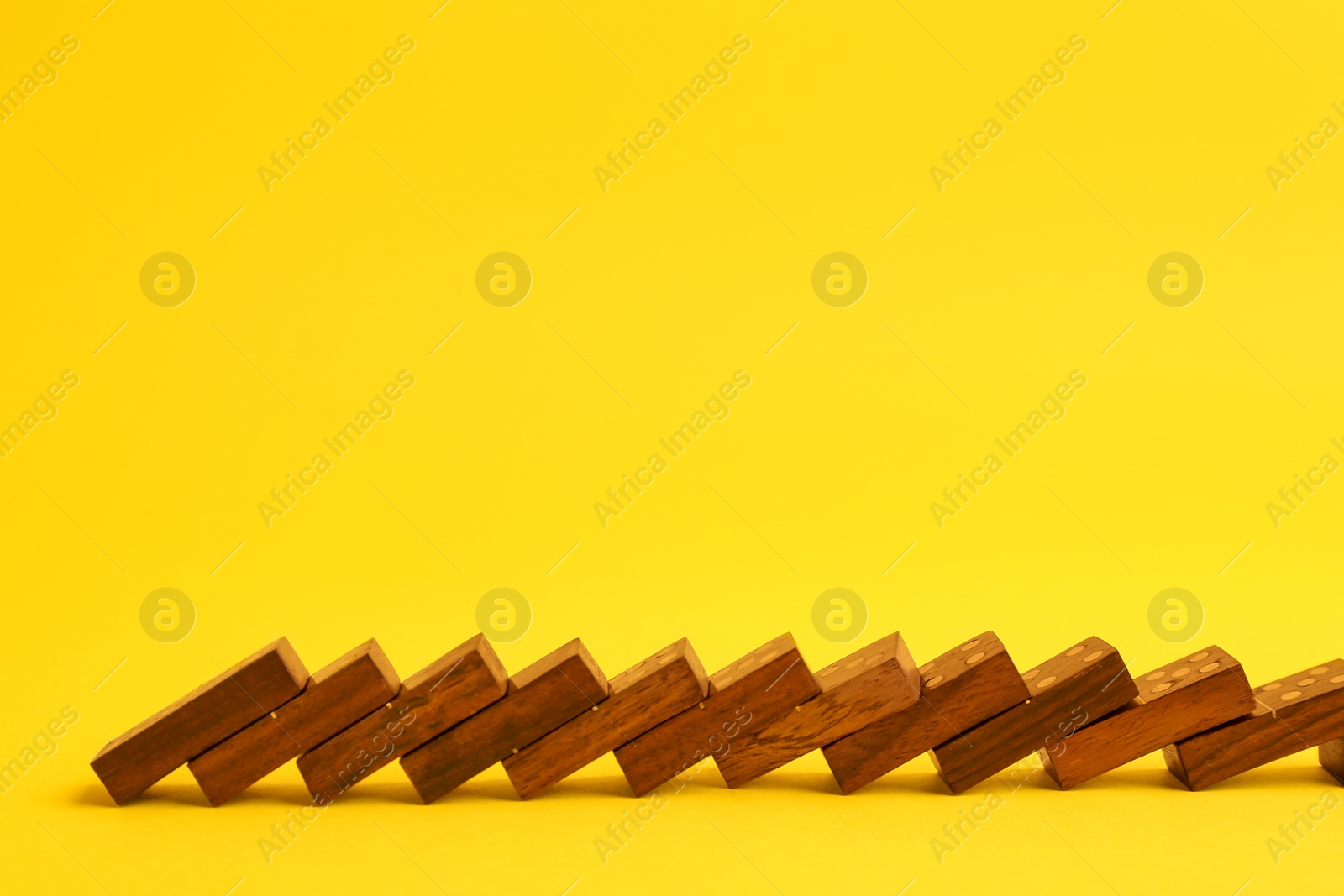 Photo of Falling wooden domino tiles on yellow background. Space for text