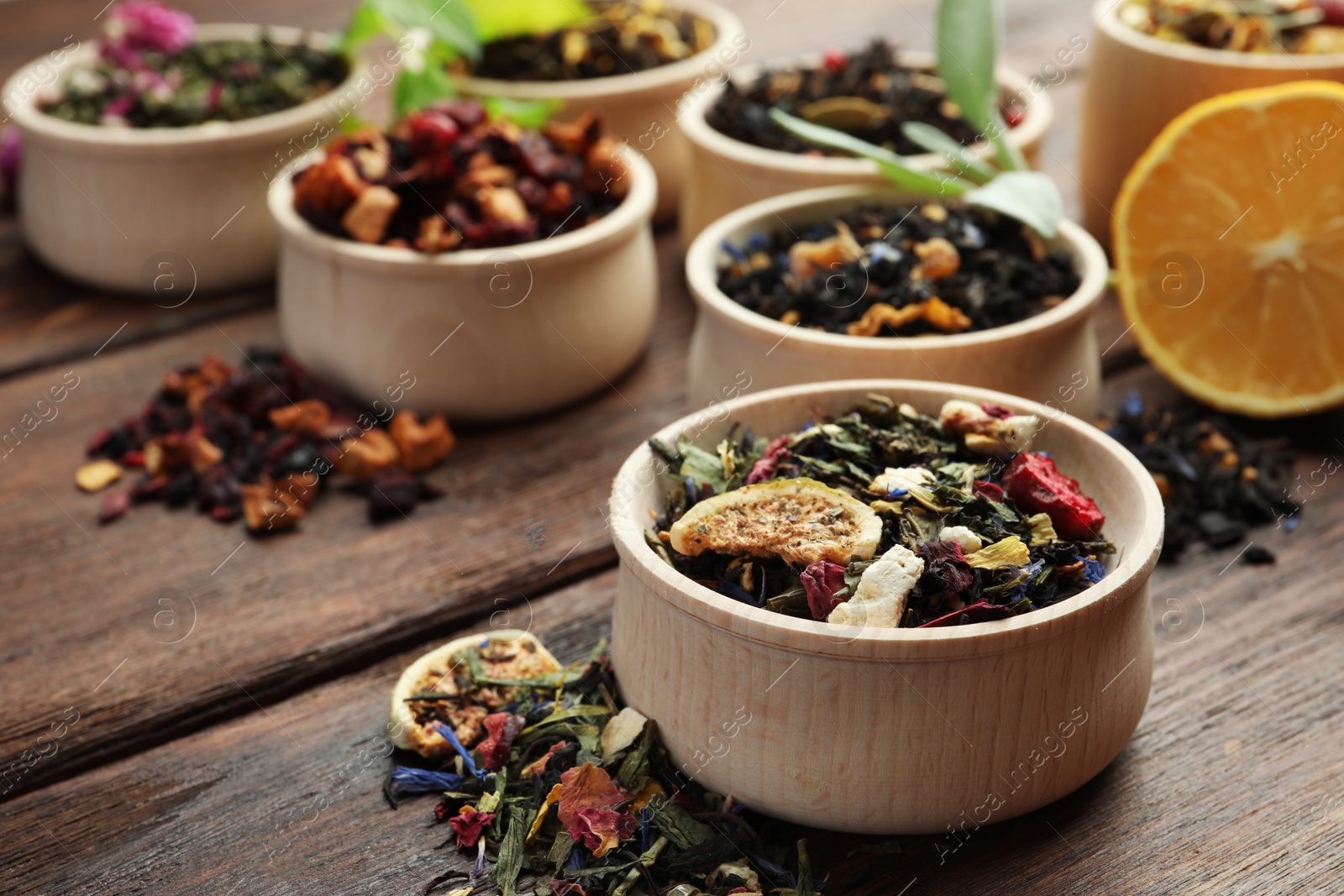 Photo of Different kinds of dry herbal tea in bowls on wooden table