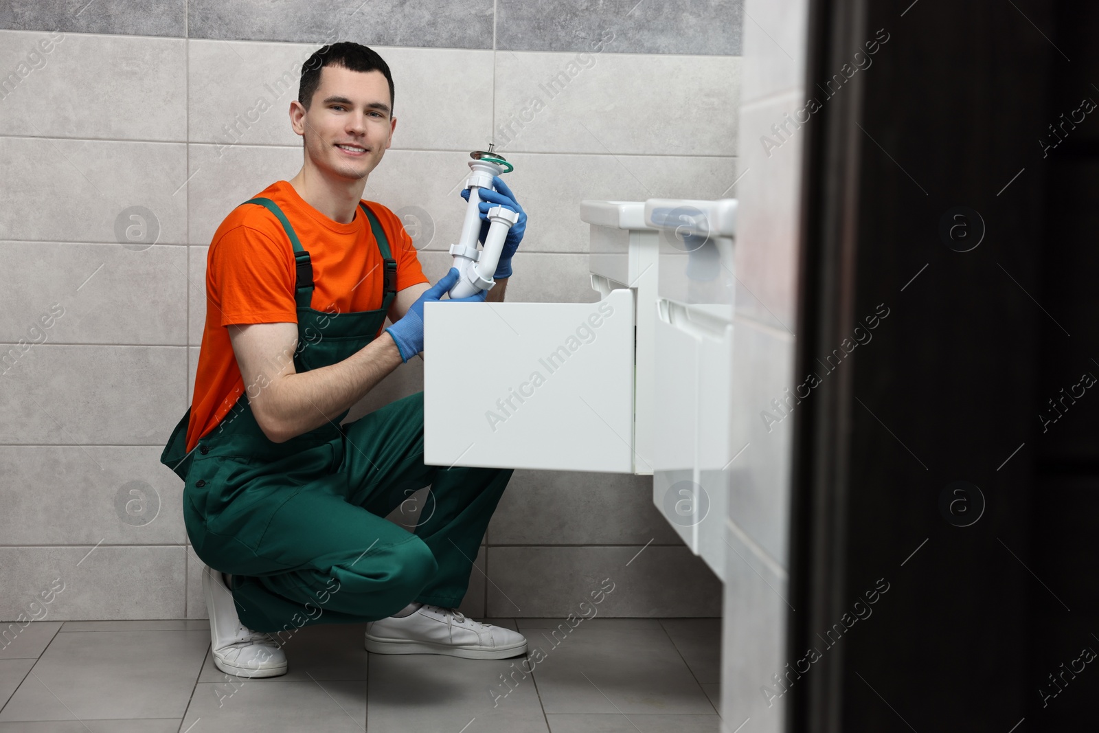 Photo of Smiling plumber wearing protective gloves repairing sink in bathroom