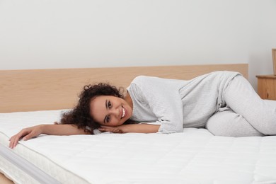 Photo of Happy young African American woman on bed with comfortable mattress at home