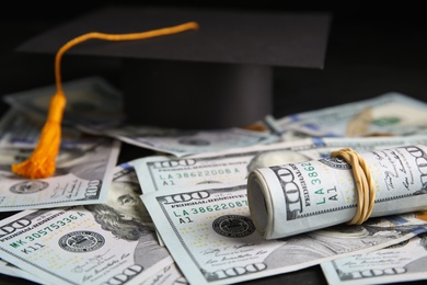 Photo of Dollar banknotes and student graduation hat on table, closeup. Tuition fees concept