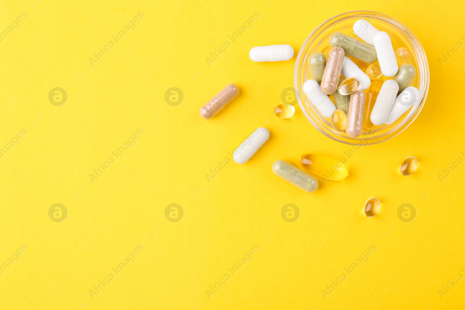 Photo of Different vitamin pills in glass bowl on yellow background, top view. Space for text