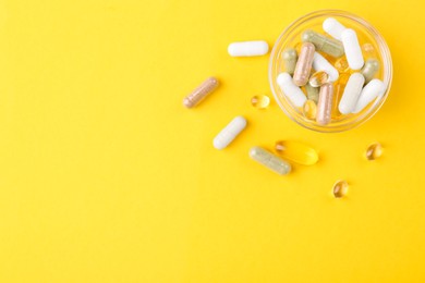 Photo of Different vitamin pills in glass bowl on yellow background, top view. Space for text