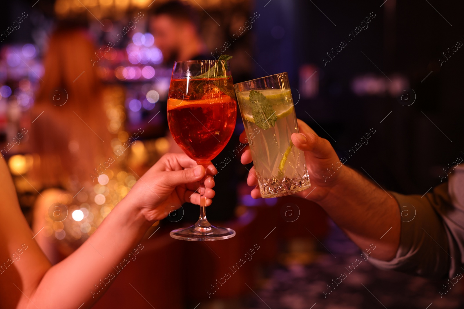 Photo of People clinking glasses with fresh cocktails in bar, closeup